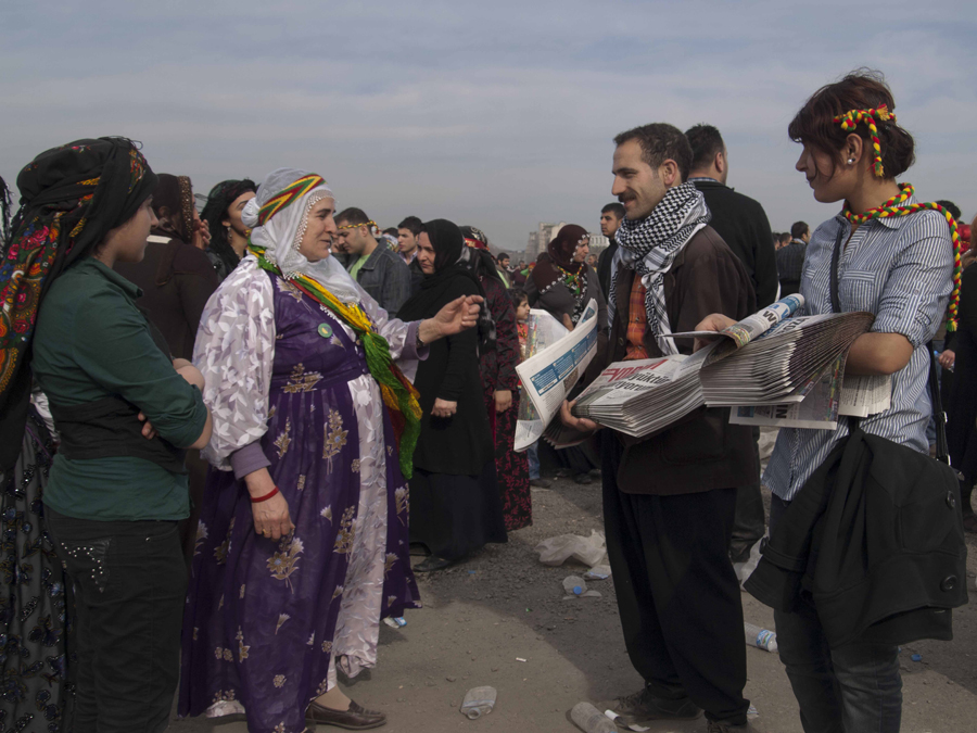 Bu karedeki bayraklar saymakla bitmez. Bir tanesi öndeki genç erkeğin boynuna sarılmış; diğeri, yanındaki genç kadının başının etrafında; bir üçüncüsü desteyle her ikisinin kucaklarında ve sonuncusu onlara uzanan yaşlı kadının ellerinde, gülüşünde...